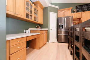 Kitchen with stainless steel fridge, glass insert cabinets, light wood finished floors, light countertops, and built in study area