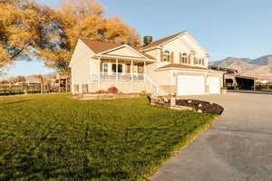 View of front of property featuring covered porch, a front yard, driveway, an attached garage, and a mountain view
