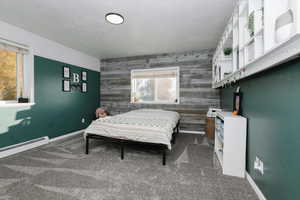Bedroom featuring a textured ceiling, carpet, an accent wall, and wood walls