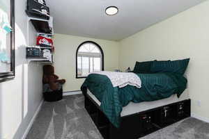 Bedroom featuring dark carpet, a baseboard radiator, and a textured ceiling