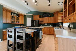Kitchen featuring lofted ceiling, open shelves, glass insert cabinets, black appliances, and a kitchen bar