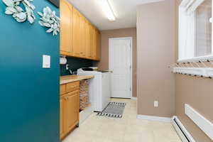 Laundry area with a baseboard radiator, cabinet space, and separate washer and dryer