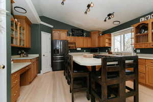 Kitchen with glass insert cabinets, vaulted ceiling, light wood finished floors, black fridge with ice dispenser, and light countertops