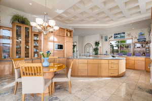 Kitchen featuring coffered ceiling, a large island with sink, recessed lighting, open shelves, and hanging light fixtures