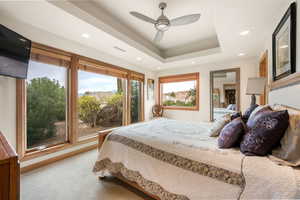 Carpeted bedroom featuring a raised ceiling, a ceiling fan, and recessed lighting