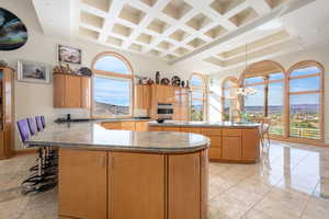Kitchen with dark stone countertops, a peninsula, a breakfast bar, coffered ceiling, and decorative light fixtures