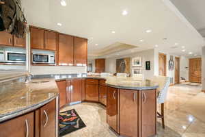 Kitchen with light stone countertops, brown cabinetry, a breakfast bar, recessed lighting, and a peninsula