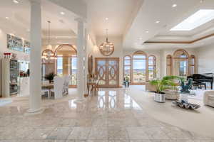 Entrance foyer featuring a tray ceiling, a chandelier, recessed lighting, ornate columns, and a high ceiling
