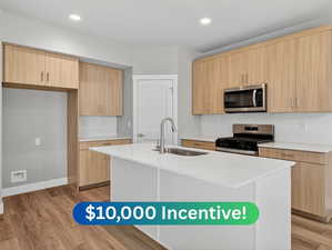 Kitchen with decorative backsplash, light stone counters, modern cabinets, appliances with stainless steel finishes, and a kitchen island with sink