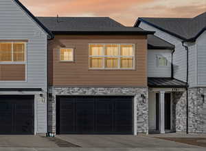 View of front of house featuring stone siding, concrete driveway, an attached garage, a shingled roof, and a standing seam roof