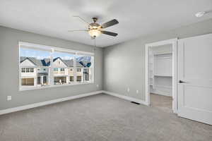 Unfurnished bedroom with light carpet, a walk in closet, a textured ceiling, and ceiling fan