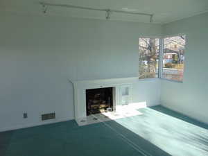 Unfurnished living room featuring track lighting, carpet flooring, and a fireplace with flush hearth