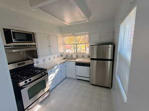 Kitchen featuring appliances with stainless steel finishes, light countertops, plenty of natural light, and white cabinets