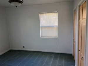Unfurnished room featuring dark colored carpet and baseboards