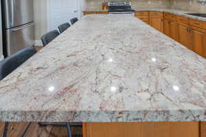Kitchen with a breakfast bar, stainless steel appliances, decorative backsplash, and light stone counters