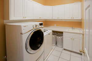 Laundry area featuring light tile patterned floors, washer and clothes dryer, and cabinet space