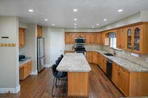 Kitchen with a kitchen bar, a textured ceiling, brown cabinets, recessed lighting, and stainless steel appliances