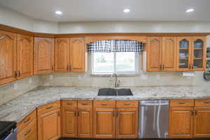Kitchen featuring light stone counters, dishwasher, brown cabinetry, decorative backsplash, and recessed lighting