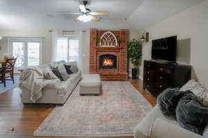 Living area with dark wood finished floors, a fireplace, a ceiling fan, and lofted ceiling