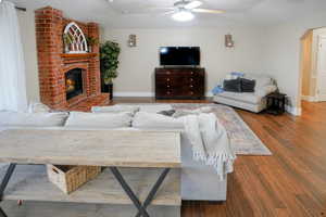 Living area with arched walkways, wood finished floors, a ceiling fan, and a brick fireplace