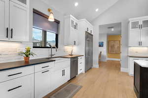 Kitchen featuring glass insert cabinets, tasteful backsplash, white cabinetry, light wood-type flooring, and stainless steel appliances