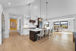 Kitchen featuring white cabinets, glass insert cabinets, tasteful backsplash, a breakfast bar, and high vaulted ceiling
