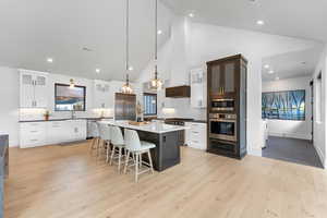 Kitchen featuring high vaulted ceiling, white cabinets, pendant lighting, and light wood-type flooring