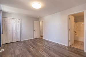 Unfurnished bedroom with dark wood-style floors, a closet, a textured ceiling, and connected bathroom