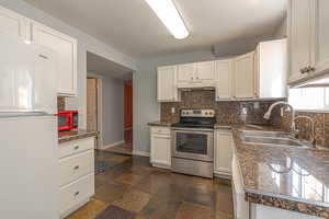 Kitchen with electric range, freestanding refrigerator, white cabinetry, decorative backsplash, and under cabinet range hood