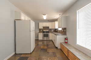 Kitchen with white appliances, white cabinetry, decorative backsplash, dark countertops, and dark stone finish floors