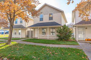 View of front of house with a porch, a front lawn, and roof with shingles