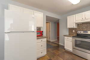 Kitchen featuring freestanding refrigerator, stainless steel range with electric stovetop, white cabinets, under cabinet range hood, and stone tile floors