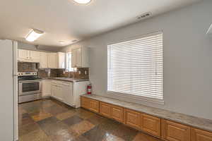 Kitchen featuring white appliances, decorative backsplash, white cabinetry, dark stone counters, and under cabinet range hood