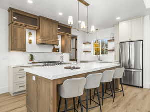 Kitchen with open shelves, brown cabinets, pendant lighting, freestanding refrigerator, and a center island