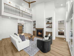 Living room with a ceiling fan, a high ceiling, built in features, recessed lighting, and a glass covered fireplace