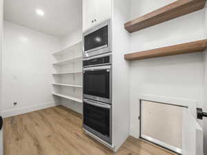 Kitchen with appliances with stainless steel finishes, light wood finished floors, white cabinets, and recessed lighting