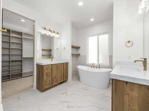 Bathroom featuring two vanities, recessed lighting, a freestanding tub, light marble finish floors, and a walk in closet
