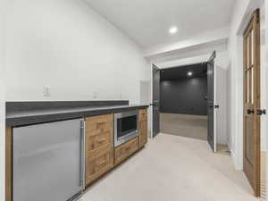 Bar with light carpet, stainless steel appliances, recessed lighting, brown cabinets, and dark stone countertops