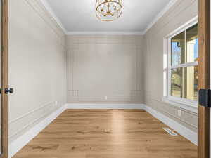 Unfurnished room with light wood-type flooring, crown molding, a chandelier, and a decorative wall
