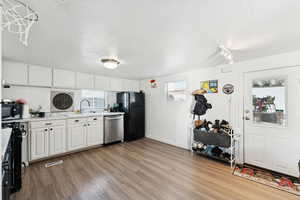 Kitchen featuring light countertops, white cabinetry, black appliances, light wood-type flooring, and backsplash