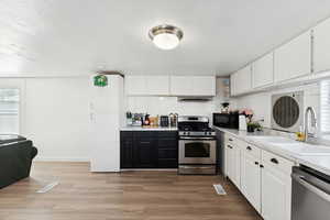 Kitchen with white cabinetry, stainless steel appliances, dark wood-style flooring, and decorative backsplash
