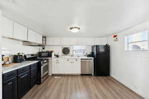Kitchen with black appliances, healthy amount of natural light, light wood-style flooring, and white cabinets
