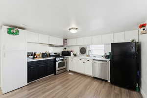 Kitchen with white cabinetry, black appliances, light wood-style flooring, and light countertops