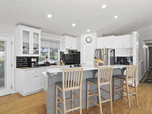 Kitchen featuring a kitchen island with sink, tasteful backsplash, white cabinetry, light wood-style flooring, and recessed lighting