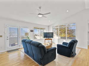 Living area featuring light wood flooring, natural light, vaulted ceiling, a ceiling fan, and recessed lighting, open floor plan, huge patio with lake / sunset views.