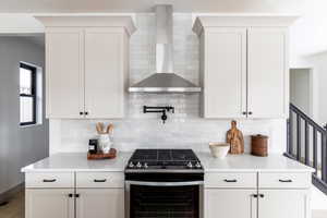 Kitchen with stainless steel gas stove, wall chimney range hood, tasteful backsplash, and white cabinetry