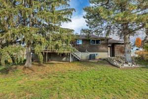 Back of house featuring stairway, brick siding, a yard, and a wooden deck