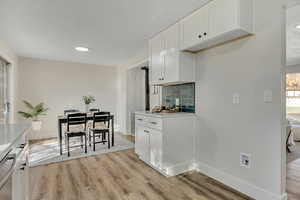 Kitchen with white cabinetry, backsplash, light wood-style flooring, dishwasher, and recessed lighting
