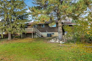 Rear view of house with stairway, a wooden deck, a lawn, brick siding, and a patio area