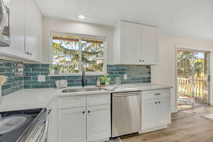 Kitchen with white cabinets, appliances with stainless steel finishes, backsplash, light wood-style floors, and light stone counters